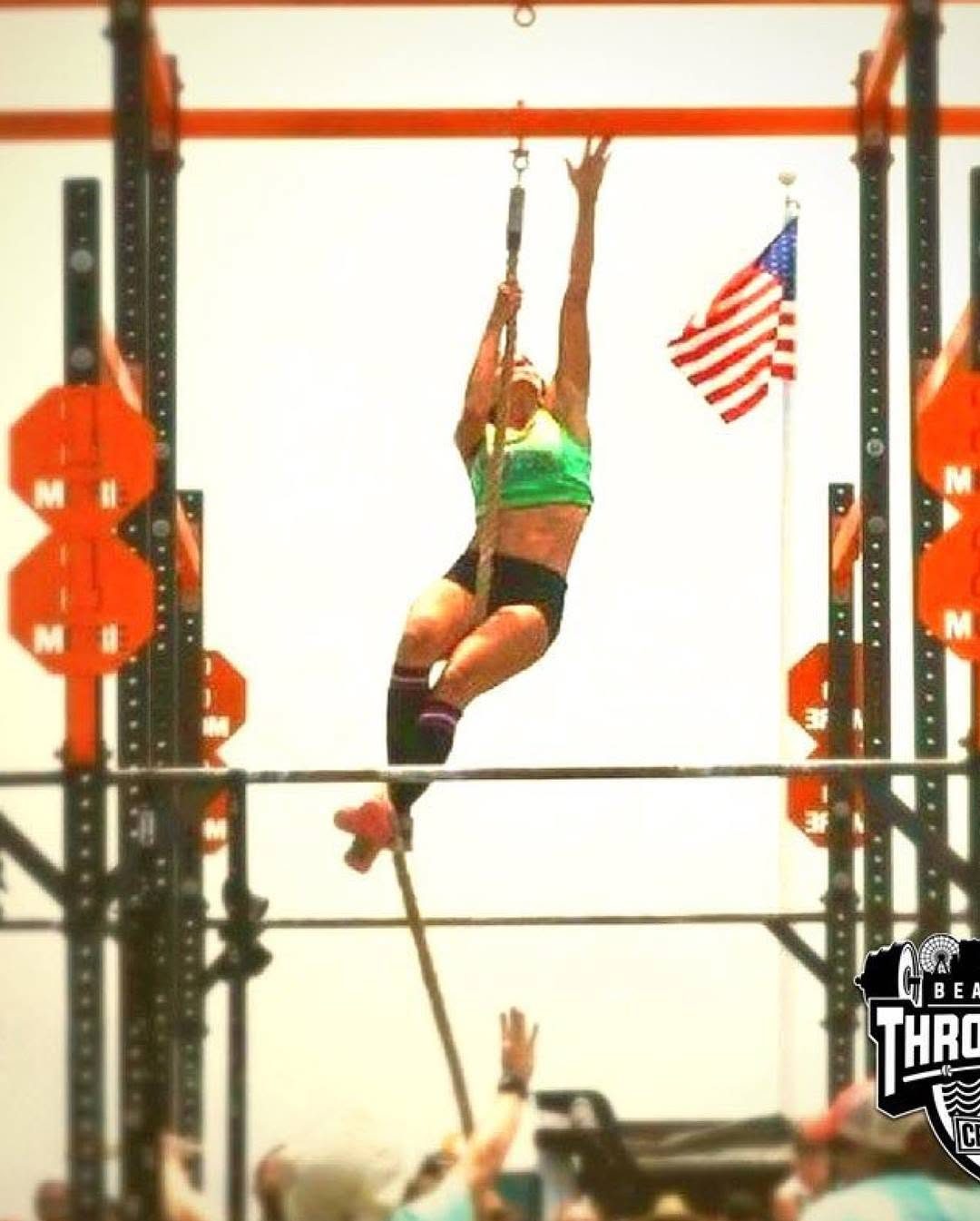 A masters athlete at the top of a rope climb under the American flag